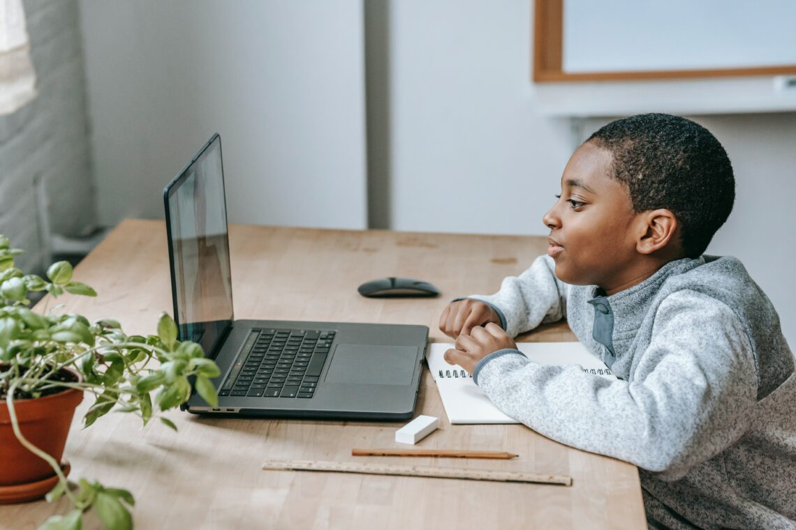 a young lad on his laptop with school supplies on his desk